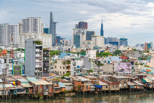 HO CHI MINH, VIETNAM - December 3, 2022: Slum wooden house on the Saigon river bank, in front of modern buildings in ho chi minh city. View to district 1, see Bitexco tower, Landmark 81.