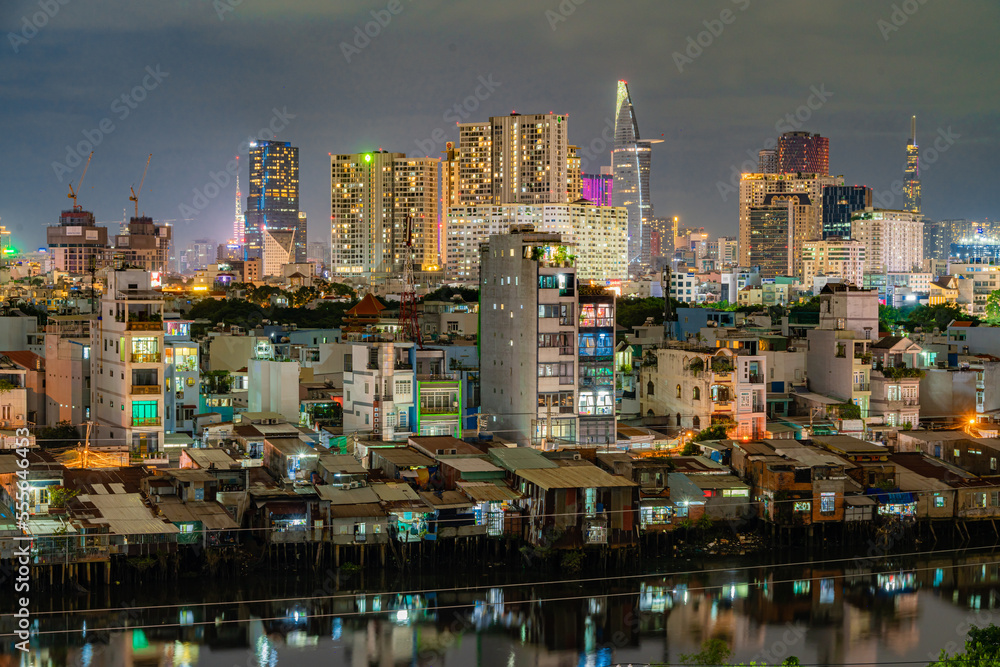 HO CHI MINH, VIETNAM - December 3, 2022: Slum wooden house on the Saigon river bank, in front of modern buildings at night in ho chi minh city. View to district 1, see Bitexco tower, Landmark 81. HO CHI MINH, VIETNAM - December 3, 2022: Slum wooden house on the Saigon river bank, in front of modern buildings at night in ho chi minh city. View to district 1, see Bitexco tower, Landmark 81.