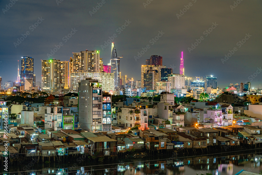 HO CHI MINH, VIETNAM - December 3, 2022: Slum wooden house on the Saigon river bank, in front of modern buildings at night in ho chi minh city. View to district 1, see Bitexco tower, Landmark 81. HO CHI MINH, VIETNAM - December 3, 2022: Slum wooden house on the Saigon river bank, in front of modern buildings at night in ho chi minh city. View to district 1, see Bitexco tower, Landmark 81.