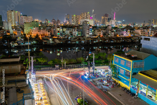 HO CHI MINH, VIETNAM - December 3, 2022: Slum wooden house on the Saigon river bank, in front of modern buildings at night in ho chi minh city. View to district 1, see Bitexco tower, Landmark 81.