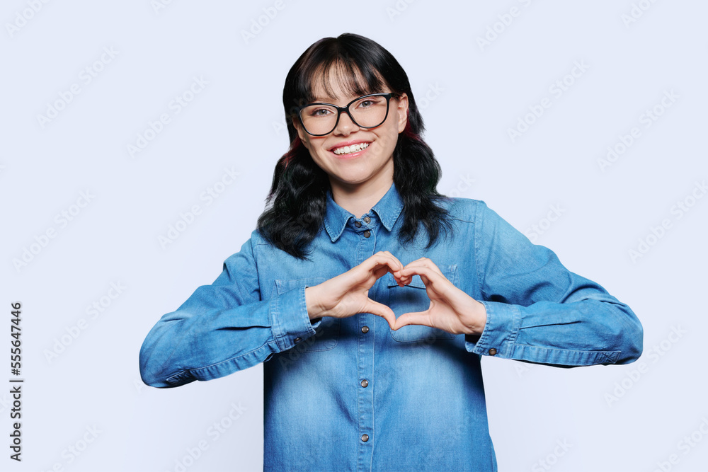 Smiling teenage female showing heart with hands on white background Smiling teenage female showing heart with hands on white background