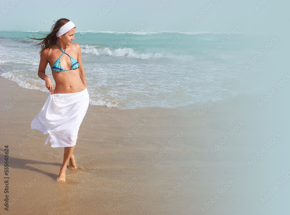 Beautiful happy girl walks barefoot, on sandy beach, along ocean, wind is blowing her hair and white skirt. Concept of travel, relaxation, happiness and freedom, copy space Beautiful happy girl walks barefoot, on sandy beach, along ocean, wind is blowing her hair and white skirt. Concept of travel, relaxation, happiness and freedom, copy space