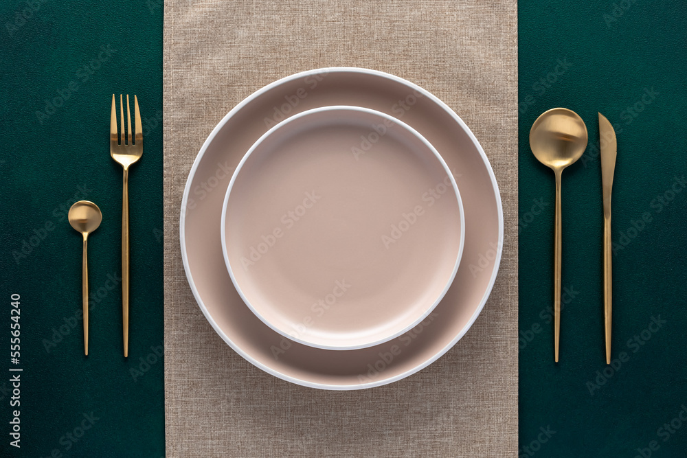 Festive place setting with beige napkin. Empty plates and gold cutlery on dark green background. Top view. Dining table in luxury restaurant. Card or menu template, flat design. Tableware, crockery. - obrazy, fototapety, plakaty 