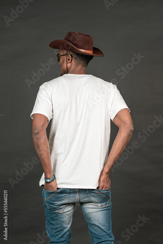 Back side of an african man wearing a white blank shirt doing a pose on the black background