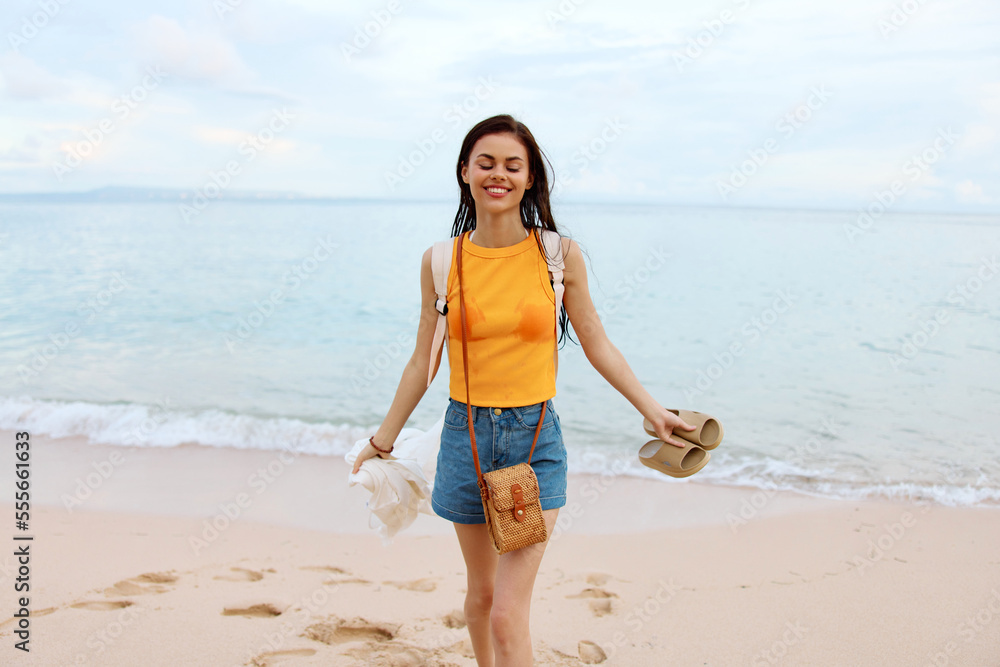 Young woman smile with teeth after swimming in the ocean with a backpack in wet clothes walking along the beach, summer vacation on the island by the ocean in Bali sunset Young woman smile with teeth after swimming in the ocean with a backpack in wet clothes walking along the beach, summer vacation on the island by the ocean in Bali sunset