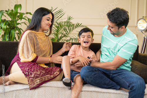 focus on mother, Happy smiling couples playing with kid by tickling or cuddling on sofa at home - concept of family bonding, affectionate and relationship photo