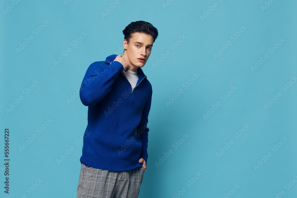 Fototapeta premium photo of a handsome, stylish man in a blue zip-up jacket standing on a light blue background adjusting the collar with his hands