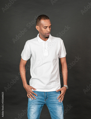 An african man with blank white polo shirt doing a pose while touching his waist on the black background