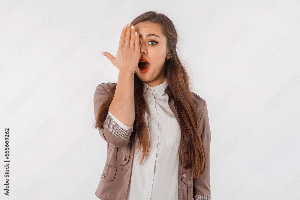 Portrait of shocked brunette girl, covering half of face, looks with one eye at camera with amazed face, holds palm on one side of face, standing over white background Portrait of shocked brunette girl, covering half of face, looks with one eye at camera with amazed face, holds palm on one side of face, standing over white background