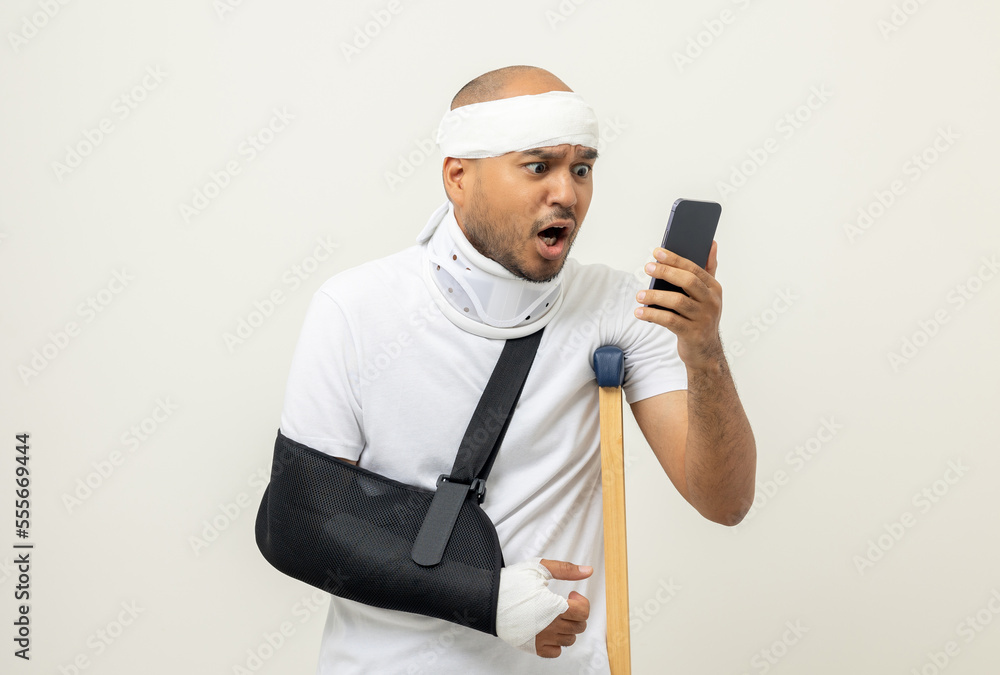 Depressed upset man suffering from pain. Broken arm. Asian man put on plaster bandage cast splint with cellphone. Patient wearing sling support arm after accident injury. life insurance and accident Depressed upset man suffering from pain. Broken arm. Asian man put on plaster bandage cast splint with cellphone. Patient wearing sling support arm after accident injury. life insurance and accident