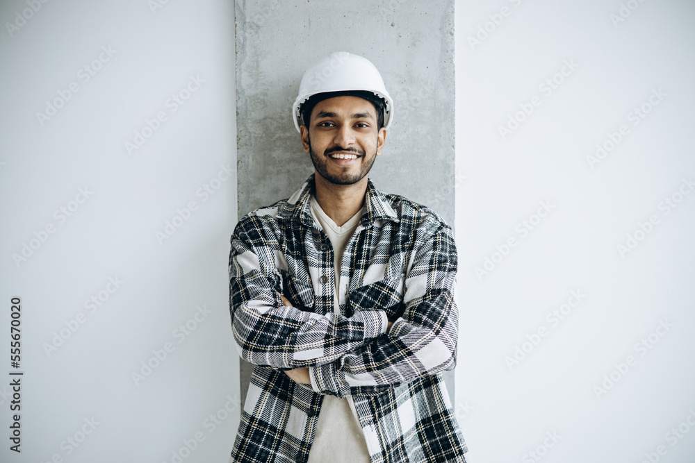 Indian workman wearing white hard hat standing isolated on gray background