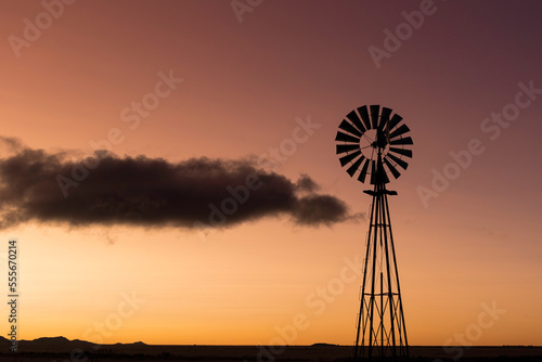 The silhouette of a windmill at sunset with an orange sky and a dark cloud drifting by.