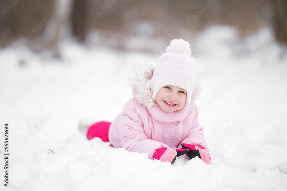 Smiling beautiful little girl lying down on white snow at city park. Cute 3 years old toddler enjoying cold winter day. Front view. Closeup. Posing and looking at camera. Smiling beautiful little girl lying down on white snow at city park. Cute 3 years old toddler enjoying cold winter day. Front view. Closeup. Posing and looking at camera.