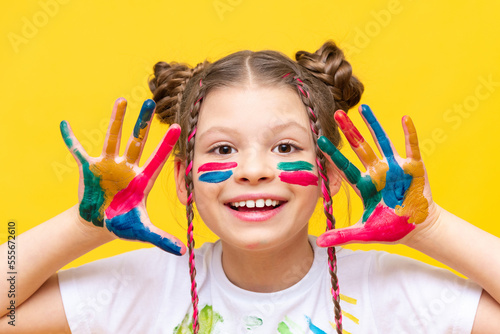 A teenage girl  smeared with multicolored paint  shows her palms and smiles broadly. The art of drawing for schoolchildren. Courses in freehand drawing. Colors of life.