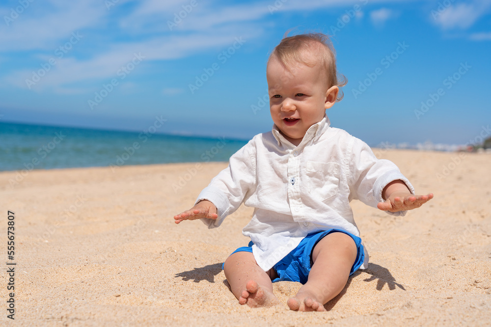 Little happy barefoot boy child sits on the beach and plays with sand on a sunny day. Little happy barefoot boy child sits on the beach and plays with sand on a sunny day.