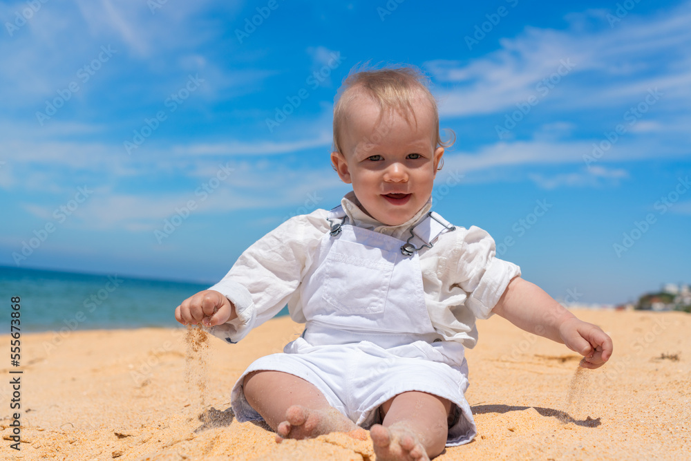 Little happy barefoot boy child sits on the beach and plays with sand on a sunny day. Little happy barefoot boy child sits on the beach and plays with sand on a sunny day.