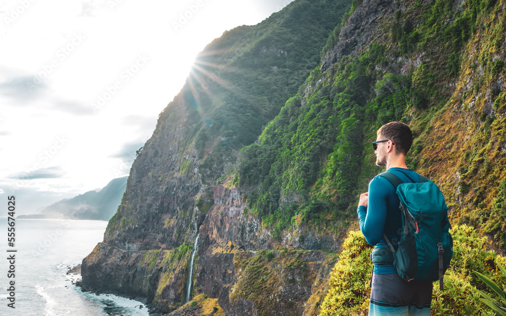 Naklejka premium Sporty man looking at waterfall flowing into the sea in atmospheric morning atmosphere. Viewpoint Véu da Noiva, Madeira Island, Portugal, Europe.