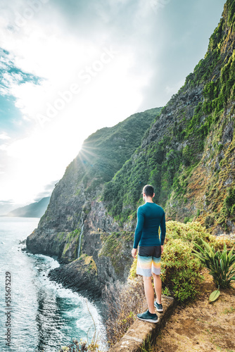 Sporty man looking at waterfall flowing into the sea in atmospheric morning atmosphere. Viewpoint Véu da Noiva, Madeira Island, Portugal, Europe.