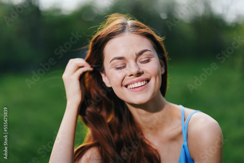 A woman in the spring nature smile with teeth touching hand long natural hair and happy, the concept of a healthy body and healthy hair in the spring and summer in the sun