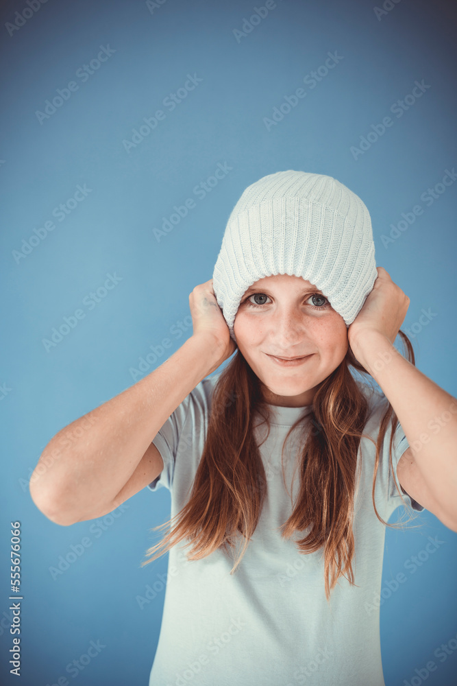 cool and pretty girl with winter wool beanie is standing in front of blue background and making grimaces, faces cool and pretty girl with winter wool beanie is standing in front of blue background and making grimaces, faces