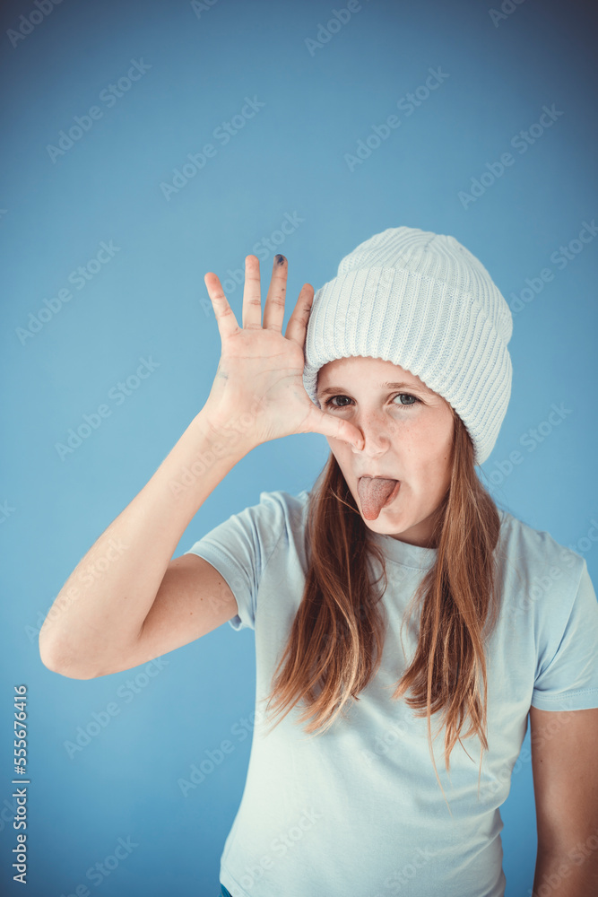 cool and pretty girl with winter wool beanie is standing in front of blue background and making grimaces, faces cool and pretty girl with winter wool beanie is standing in front of blue background and making grimaces, faces