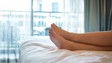 Human legs part during laying or sleeping down on the bed sheet with domestic room interior background. Holiday relaxation concept photo scene, selective focus.
