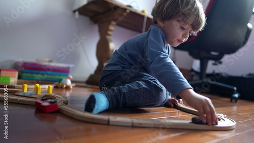 Little boy playing with toys on hardwood floor. Child plays with traditional railroad wooden tracks at home. Male kid holding objects