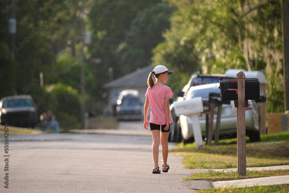 Obraz premium Rear view of confident young child girl walking along the sunny alley. Active lifestyle on summer holidays