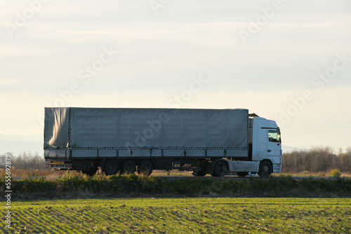 Semi-truck with cargo trailer driving on highway hauling goods in evening. Delivery transportation and logistics concept