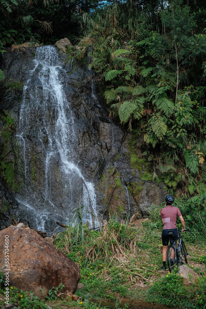A young female cyclist is carrying her bike to look at the waterfalls.