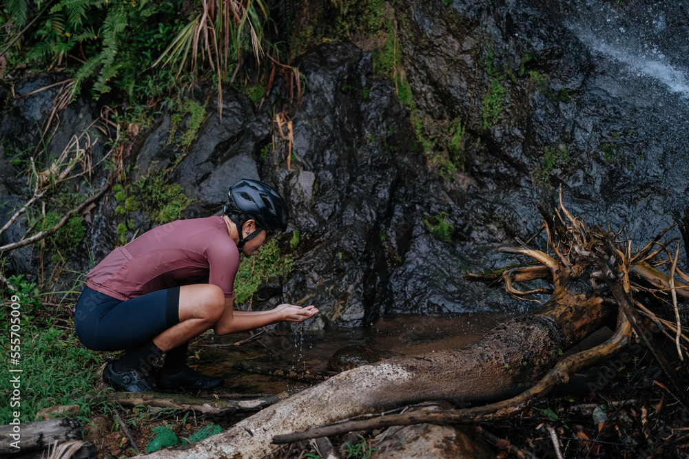 Obraz premium A young female cyclist is washing her hands by the creek