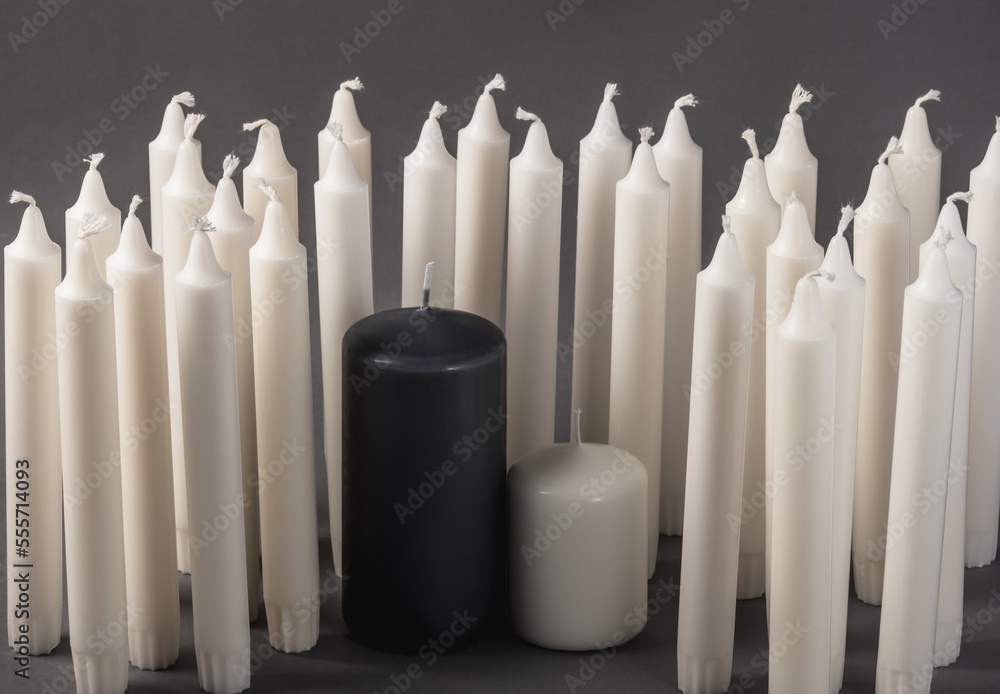 Black and white candles surrounded by many thin white candles on a dark gray background. Black and white candles surrounded by many thin white candles on a dark gray background.