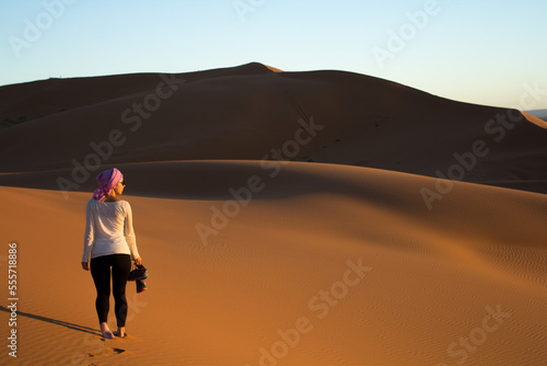 backlight of a girl walking barefoot through the sahara desert at sunset