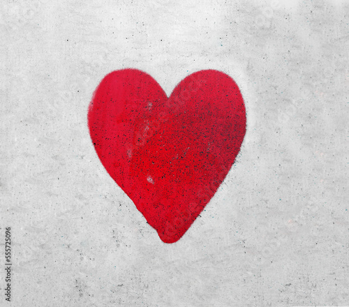 A red love heart spray painted on a wall background. heart painted on grey fence backdrop.
