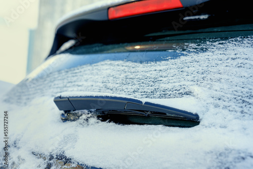 Rear window of car with black wiper covered with snow and ice on road in winter season close up back view
