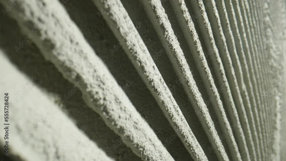 Camera movement by fresh concrete tehture with patterns of notched trowel. Macro shot of grey surface cement putty on wall with lines or strokes stripes. Uneven adhesive mortar paste for ceramic tiles Camera movement by fresh concrete tehture with patterns of notched trowel. Macro shot of grey surface cement putty on wall with lines or strokes stripes. Uneven adhesive mortar paste for ceramic tiles