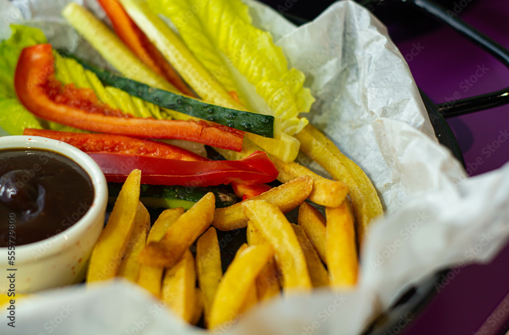 Black plate with french fries, fresh vegetables and sauce.