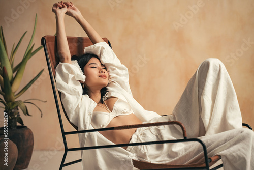 Young korean model relaxing on lounger on background with brown textured wall, stretching hands photo