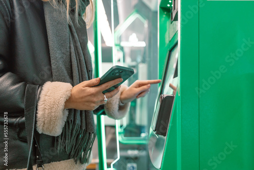 Close-up of a woman paying at a self-service machine using a contactless phone payment. Woman take a train ticket after buy from subway ticket machine. Transportation concept