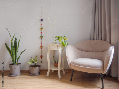 Elegante mueble de lectura beige, acompañado de maceteas con plantas y mesa blanca con lampara y adornos con fondo blanco y cortinas grises photo