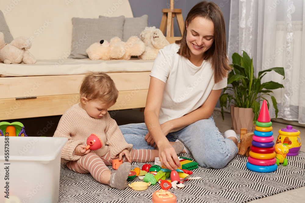 Overjoyed loving young Caucasian mother play with toys plastic fruit with small baby daughter. Happy smiling mom have fun, feel playful with little toddler kid child. Parenthood.