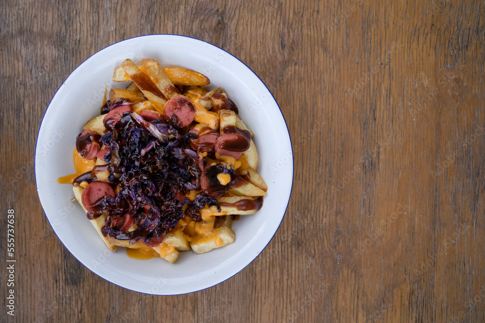 Top view of fried potatoes with sausages, red cabbage, cheddar cheese and barbecue sauce, in a white bowl with a wooden background. Top view of fried potatoes with sausages, red cabbage, cheddar cheese and barbecue sauce, in a white bowl with a wooden background.
