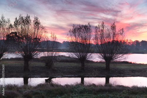 Die aufgehende Sonne taucht den Fluß, die Bäume, den Himmel und die Wolken in ein rotes Licht. photo