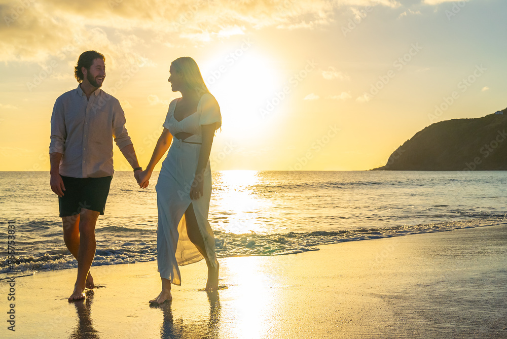 Happy couple walking along waterfront sandy beach on a tropical island during the golden hour