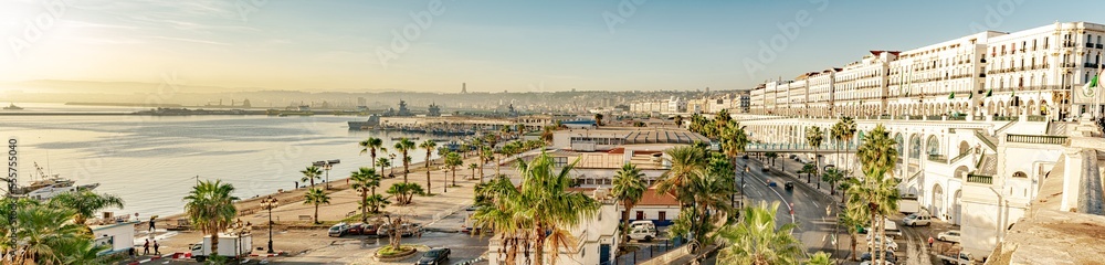 Fishery Port and the urban sea Station, bay of water, the Martyr's Memorial, Zighout Youcef Boulevard and Angkor road with white buildings. Golden hour sunlight in a blue sky.