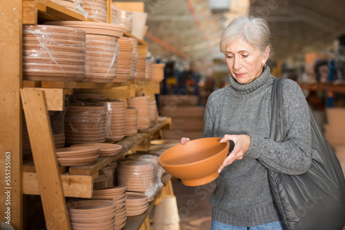 Senior caucasian woman choosing earthenware crockery in store.