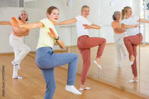Ordinary teen girl with family exercising dance moves with group of people in dance center