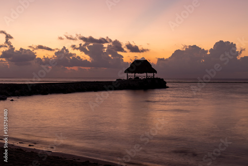silhouette d'une cabane avec un toit de paille sur la mer lors d'un lever de soleil