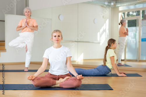 Family of three various aged women exercising yoga together in studio.