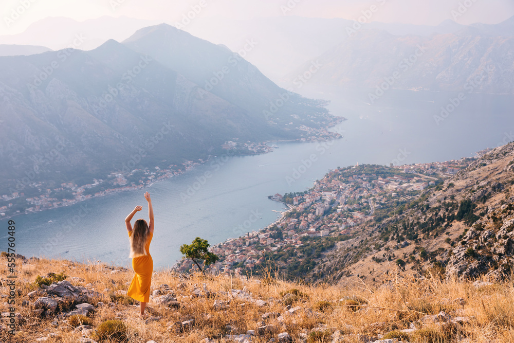 Rear view girl raises her hands up. She admires the city of Kotor in Montenegro and shows how happy she is.